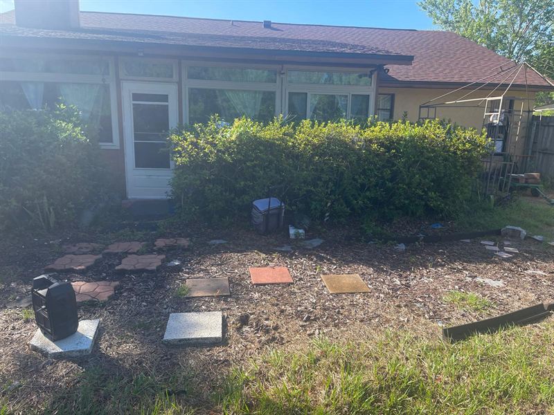 Patchy backyard bed of mismatched stepping stones and weeds outside a sunroom