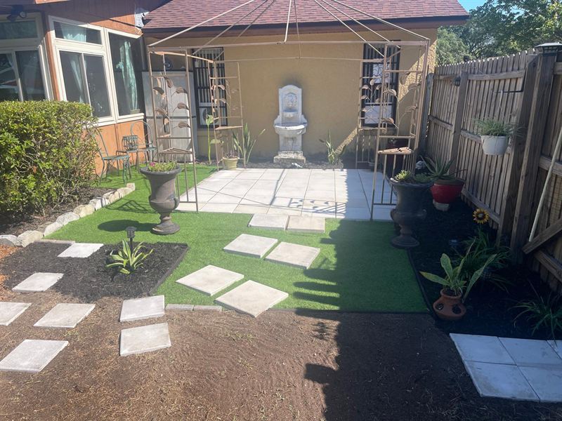 The same side yard as a finished courtyard with a paver patio, artificial turf, planters and stepping stones