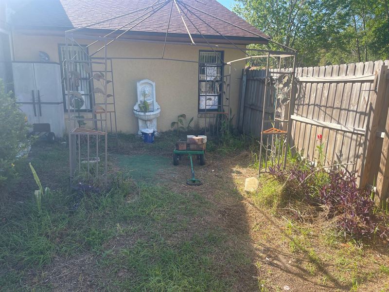 Weedy, overgrown side yard with a bare gazebo frame and a wall fountain