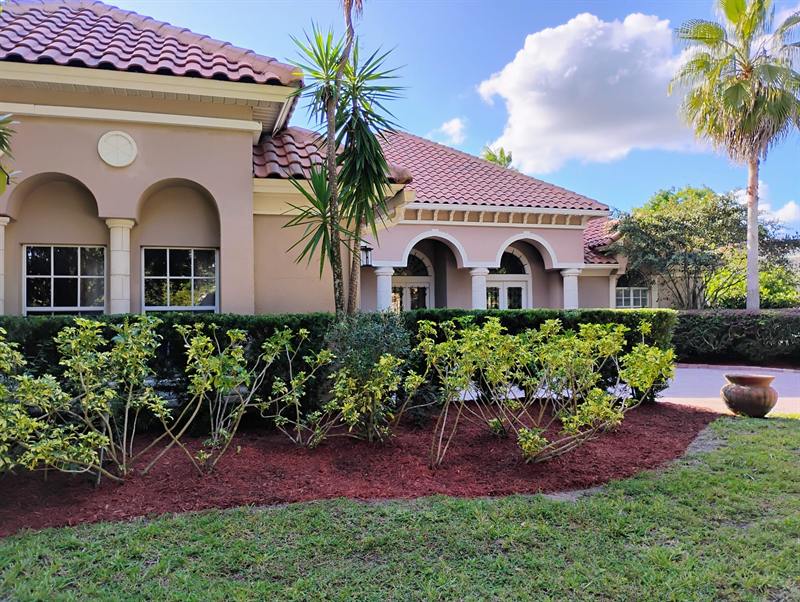 Trimmed hedges and fresh beds across the front of a large Mediterranean-style home