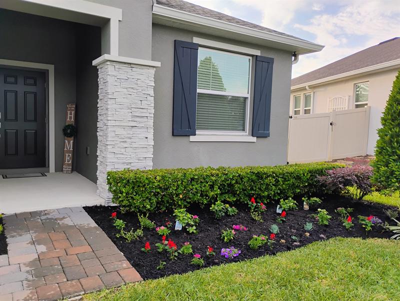 Colorful flowers and fresh mulch framing a stone-column front entry