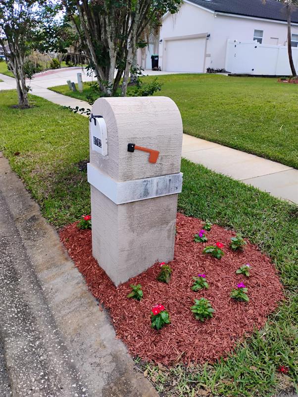 Stone mailbox pillar with red mulch and pink and red flowers