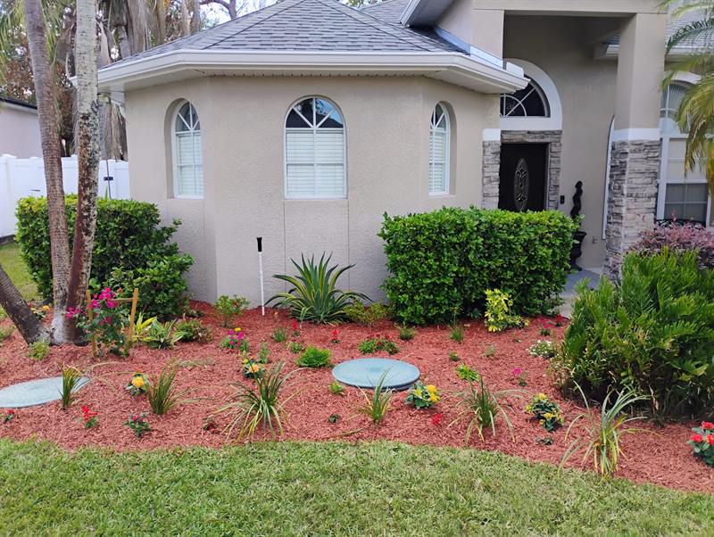 Red mulch bed with shrubs and flowers wrapping the corner of a stucco house with arched windows