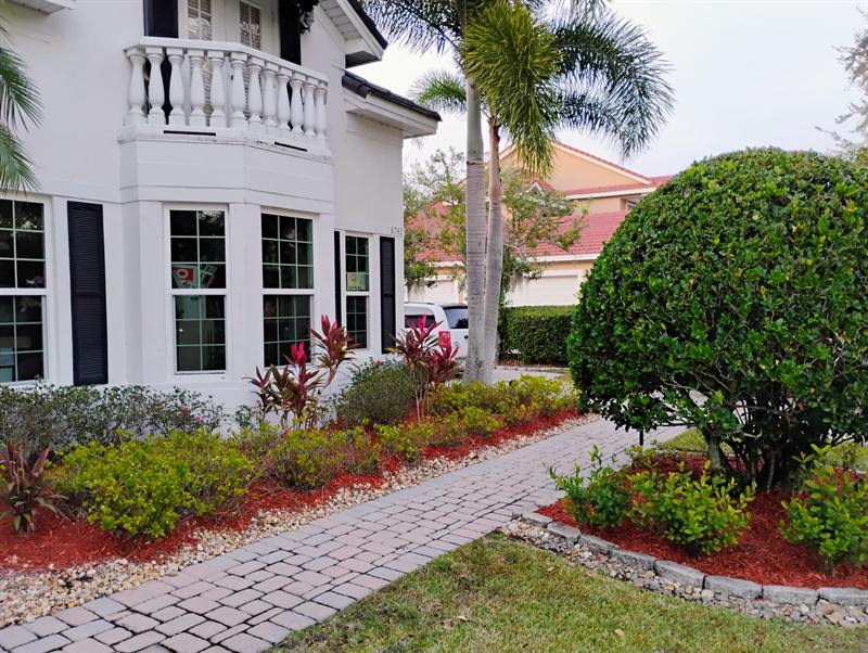 Curved paver walkway with red mulch, stone edging and a rounded topiary at a white house